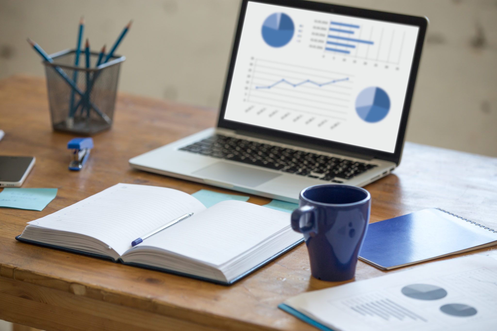 Home office interior in loft space. Workplace with wooden table, office supplies, documents, organizer and laptop. Modern office workplace. Focus on open planner book with blank pages