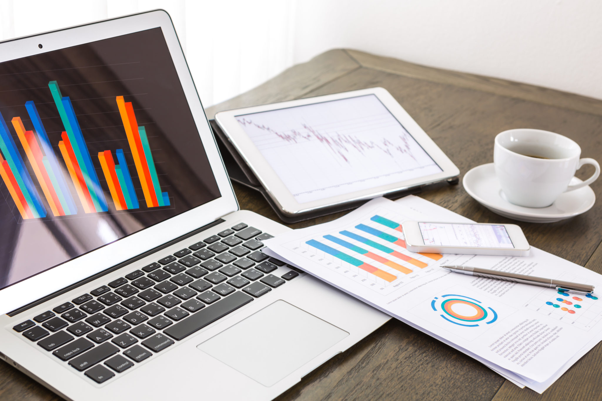 Laptop, tablet , smartphone and coffee cup with financial documents on wooden table